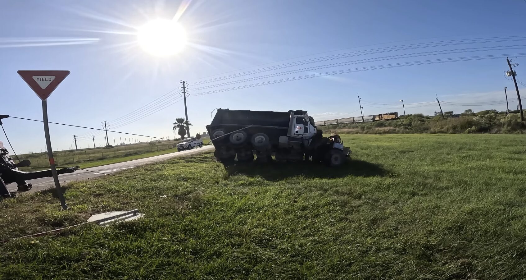 Heavy-duty truck overturned in grassy ditch beside rural highway requiring emergency recovery