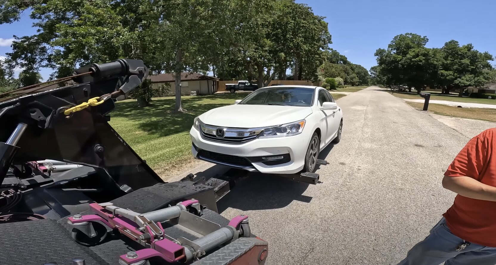 Professional tow truck operator loading a white sedan onto flatbed trailer in residential area