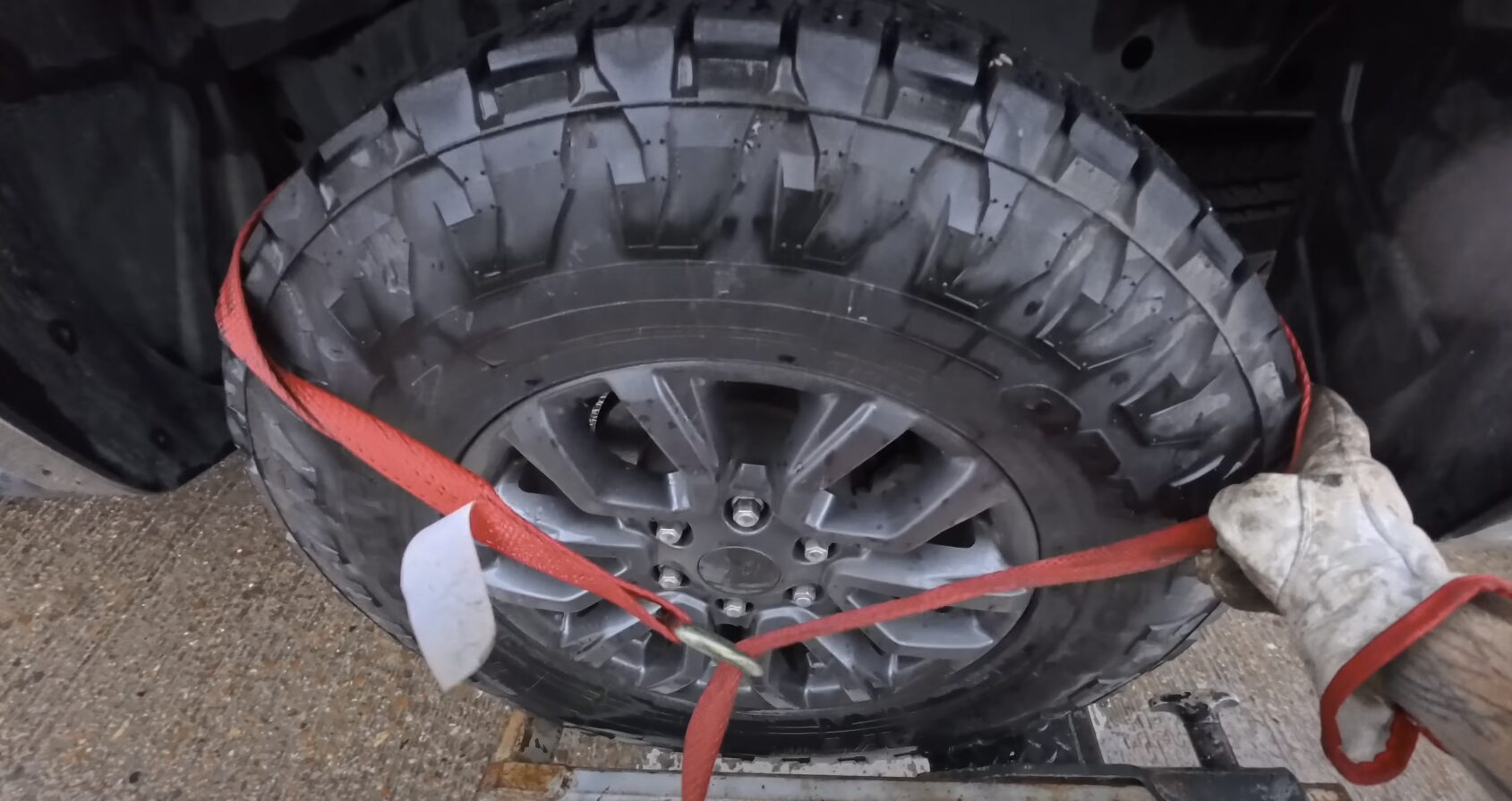 Car wheel secured with red towing straps on flatbed truck for safe transport